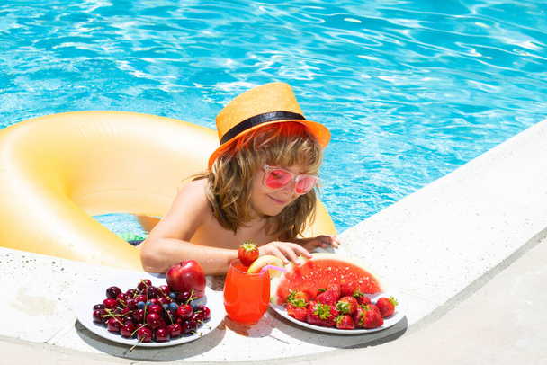 Child eating fruits near swimming pool during summer holidays. Kids eat fruit outdoors. Healthy fruits for children - Foto, Imagem