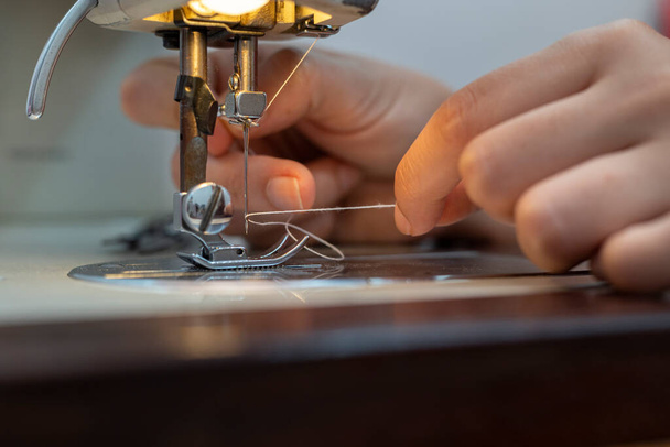 Costurera latinoamericana inserta hilo en la aguja de la máquina de coser - Foto, Imagen