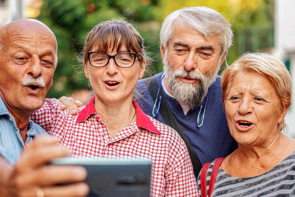 Пожилые пары делают селфи со смартфоном - Встреча старых друзей, веселящихся на открытом воздухе - Фото, изображение