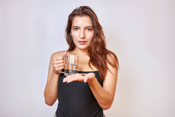 The girl holds a capsule and a glass of water in her hands. Medical devices for weight loss. - Foto, Imagen