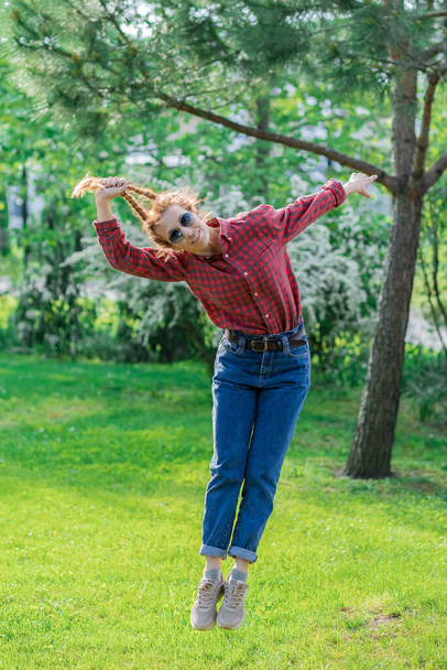 Mujer alegre tira de sí misma en el aire por coletas en el parque verde. Jugando el fin de semana. Cabello fuerte. - Foto, imagen
