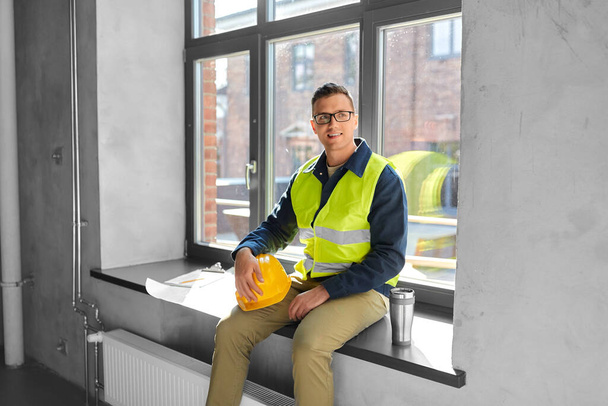 architecture, construction business and people concept - happy smiling male builder or architect with tumbler or thermo cup sitting on window sill at office - Valokuva, kuva