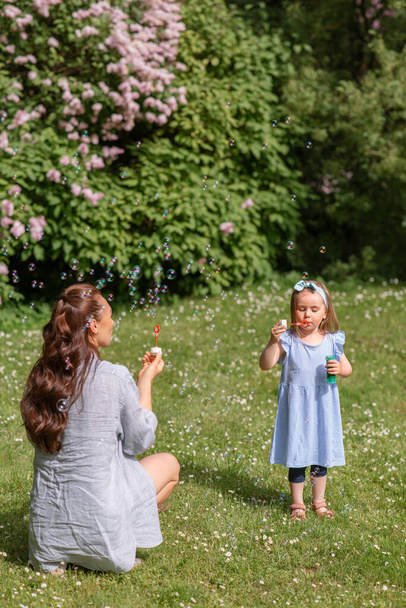 family, motherhood and people concept - happy mother with little daughter blowing soap bubbles at summer park or garden - Photo, Image