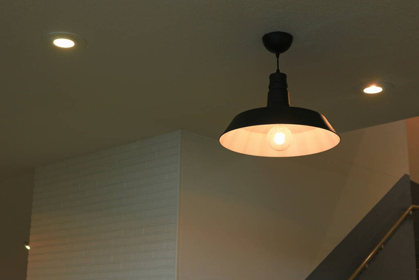 Illumination of an iron pendant lamp shade with a simple design hung in a dimly lit room - Φωτογραφία, εικόνα