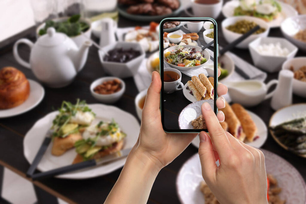 Woman taking picture of different dishes served on wooden table, closeup - Fotó, kép