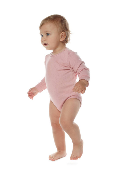Cute baby girl in pink bodysuit learning to walk on white background - Zdjęcie, obraz