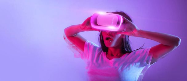Surprised millennial lady in virtual reality glasses, having great virtual experience, touching headset, mouth open, looking at free space, neon light background, web-banner, collage - Photo, Image