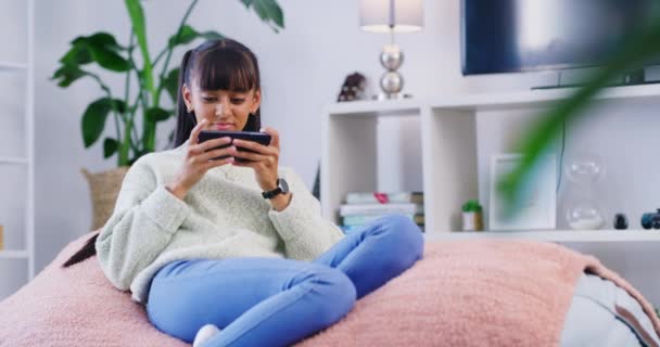 Egy tinédzser telefonál, miközben otthon pihen egy babzsákon a nappaliban. Fiatal lány játszik egy mobil játék, vagy streaming egy videót a hétvégén. Szabadidő élvezése az interneten vagy a közösségi médiában. - Felvétel, videó