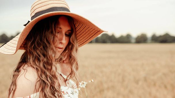 Beauty romantic girl outdoors. Happy young woman in sun hat in summer wheat field at sunset. Copy space, sunset, flare light, summer season. Boho chic style - Zdjęcie, obraz