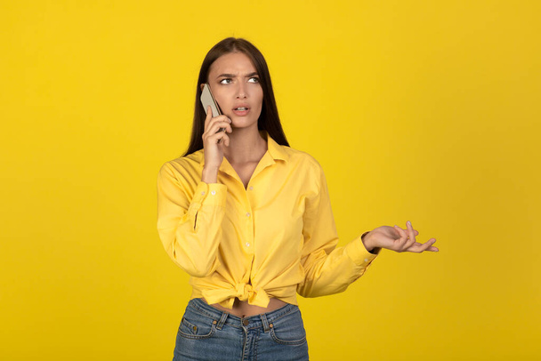 Niezadowolona Millenijna kobieta rozmawiająca przez telefon komórkowy komunikująca się nad żółtym studiem tle. Lady Wołająca o Nieprzyjemną Rozmowę Komórkową. Problem komunikacji - Zdjęcie, obraz