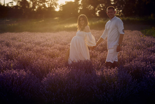 young beautiful pregnant couple walking on a lavender field at sunset. Happy family concept - Foto, afbeelding