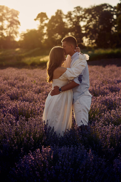 portrait of a young beautiful pregnant couple on a lavender field at sunset. Happy family concept - Fotoğraf, Görsel