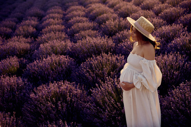 the pregnant girl with a hat in the lavender field on a sunset - Photo, image