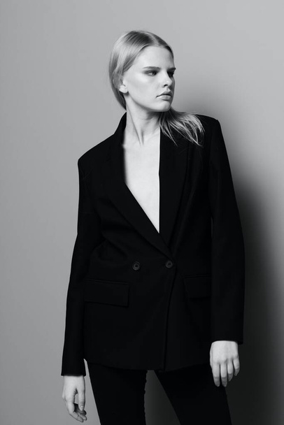 Средний портрет элегантной девушки в формальном костюме и черной куртке в студии. Черно-белый стиль. Концепция брендов одежды. Высокое качество фото - Фото, изображение