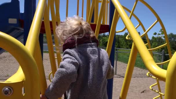 Video al rallentatore da dietro un audace bambino di 3 anni con capelli biondi ondulati, che sale sulle sbarre gialle di uno scivolo da parco giochi ambientato nel parco locale. - Filmati, video