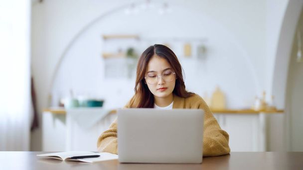 自宅のノートパソコンで働くアジアの若い女性の笑顔。コンピュータ・リモート・スタディング、バーチャル・トレーニング、 eラーニング、家でのオンライン教育のウェビナーを見ている若いアジアの学生 - 写真・画像