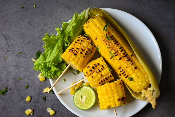 sladká kukuřice vařená na bílém talíři, sladké kukuřičné krmivo se salátem zeleninový limetkový koriandr a hlávkový salát, zralá kukuřičná kukuřice grilovaná kukuřice na jídlo veganská večeře nebo svačinka - Fotografie, Obrázek