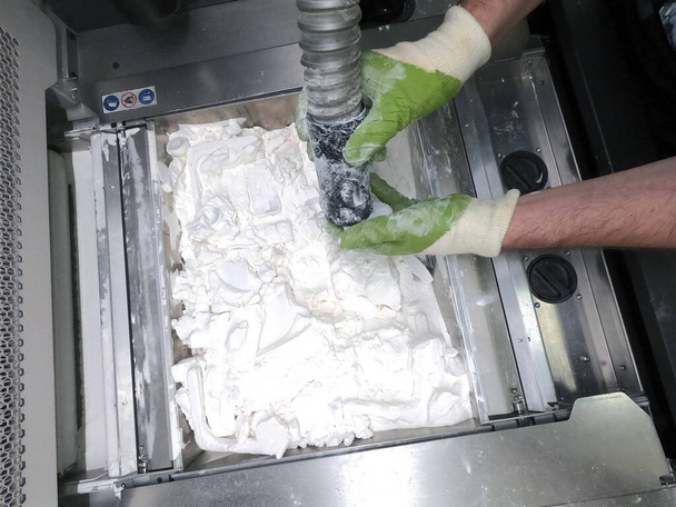A man working with a working vacuum cleaner to clean the white powder of polyamide from a model printed on a 3D printer inside a 3D printer. Cleaning objects printed on an industrial powder 3D printer - Photo, Image