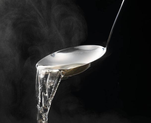 Dashi, soup stock, and the basics of Japanese cuisine. Black background. Steam. Scooping with a ladle. - Photo, image