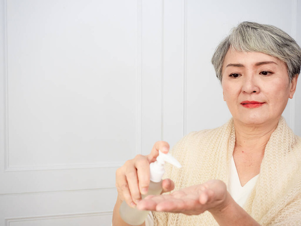 Portrait of mature asian woman 50s holds a white bottle with a cosmetic product. - Фото, зображення