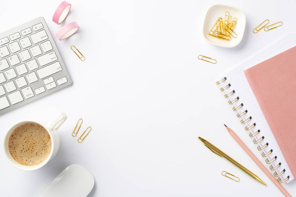 Business concept. Top view photo of workplace keyboard computer mouse cup of coffee stationery pink adhesive tape clips pens and pink planners on isolated white background with empty space - 写真・画像