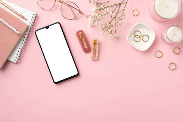 Business concept. Top view photo of workplace smartphone candles diaries pencils stylish glasses gold rings trendy barrettes and white gypsophila flowers on isolated pastel pink background - Photo, Image