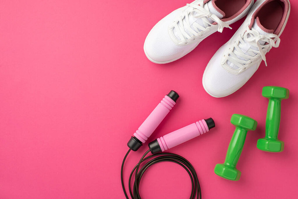 Sports accessories concept. Top view photo of white sneakers green dumbbells and skipping rope on isolated pink background - Фото, зображення