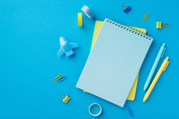 Back to school concept. Top view photo of school supplies notebooks pens adhesive tape plane shaped sharpener and binder clips on isolated blue background with empty space - Φωτογραφία, εικόνα