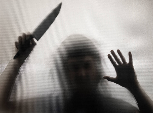 Horror, halloween background - Shadowy figure behind glass holding a knife - Foto, Imagem