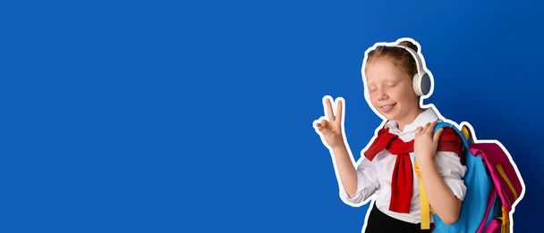 Cute little schoolgirl listening to music and showing victory gesture on blue background with space for text - Photo, Image