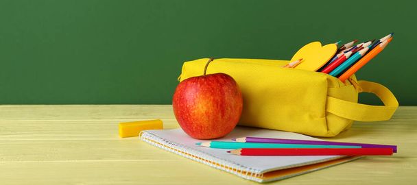 School stationery and apple on table against green background - 写真・画像