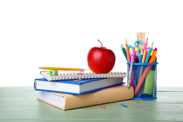 Papelería escolar con manzana y libros sobre mesa sobre fondo blanco - Foto, imagen