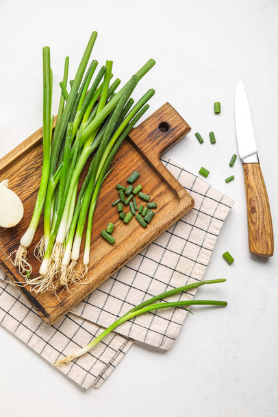 Wooden board with fresh green onion and knife on light background - Foto, afbeelding