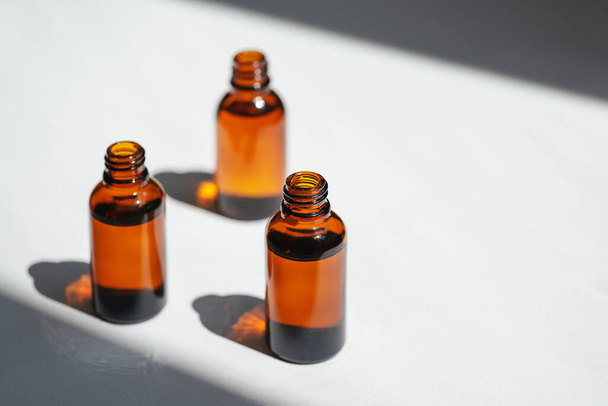 Open amber bottle with serum or essential oil. White background with daylight and beautiful shadows. Beauty concept for face and body care - Foto, Imagem