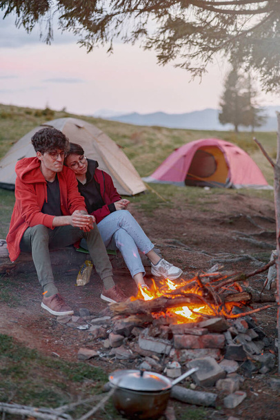 Caucasian romantic couple sitting at fire and warming up in hugs near tents. Rest at nature. Love. - Fotoğraf, Görsel