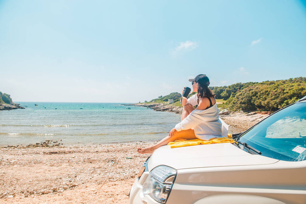 vrouw zitten aan auto kap drinken koffie genieten van uitzicht op de zee zomer vakantie - Foto, afbeelding