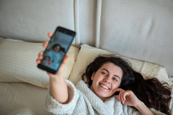 mladá šťastná žena brát selfie příběh ležící v posteli ranní čas - Fotografie, Obrázek