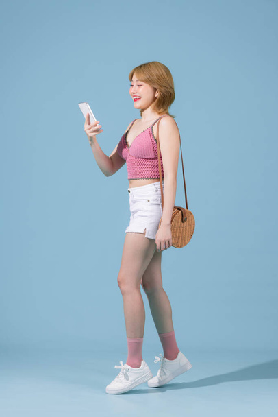 Happy young woman using mobile cell phone walking going isolated on pastel blue background studio portrait - Fotó, kép