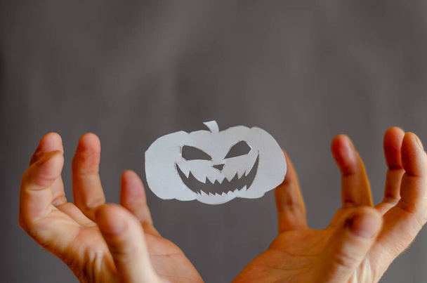 Biała księga Halloween Dynia i ręce z palcami zgiętymi w przerażeniu. Przedmioty halloweenowe pocięte nożyczkami z kartki papieru. Latanie w ir Silhouette Uśmiechnięta, onieśmielająca twarz. Ręce mężczyzny - Zdjęcie, obraz