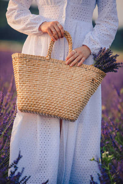 donna in abito bianco con bouquet di fiori di lavanda in sacchetto di paglia da vicino - Foto, immagini