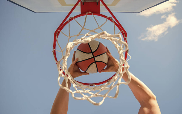 Ο μπασκετμπολίστας ρίχνει την μπάλα στο στεφάνι με φόντο τον ουρανό, στοχεύοντας. - Φωτογραφία, εικόνα