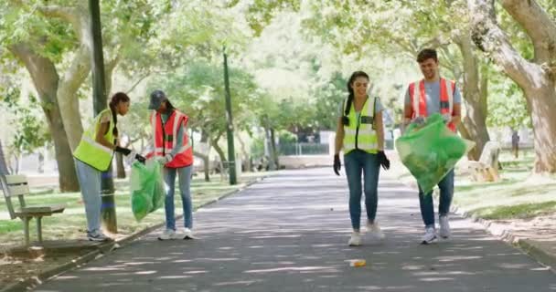 Young volunteers picking up trash together in park. Group of people carrying bags to collect garbage in a botanical garden outside. Diverse garbage collectors doing a routine cleanup at playground. - Filmmaterial, Video
