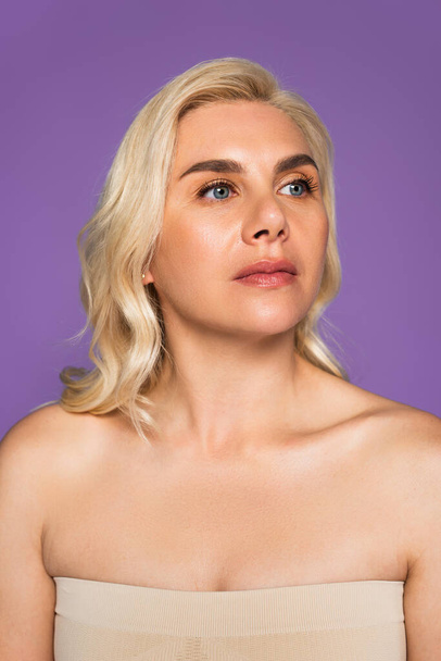 blonde woman with bare shoulders looking away isolated on purple - Fotografie, Obrázek