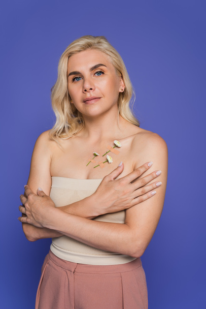 blonde woman with plasters and white flowers on body looking at camera isolated on purple - Fotografie, Obrázek