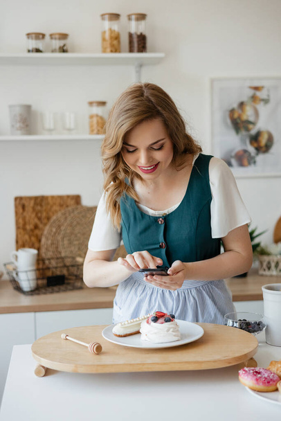 Beautiful girl confectioner takes a photo of a cake in the kitchen. High quality photo - Zdjęcie, obraz