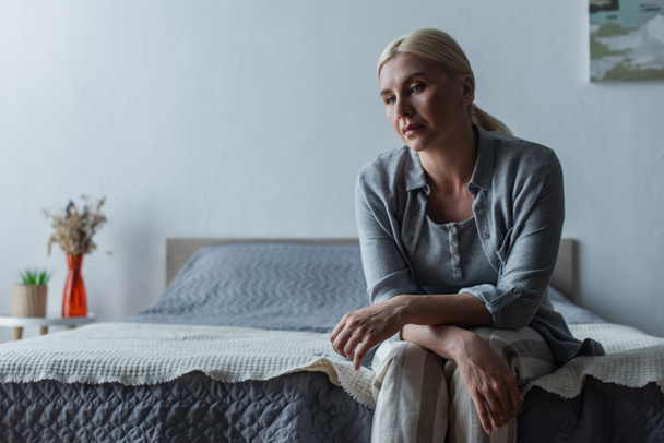 zdenerwowana blondynka z menopauzą siedząca na łóżku w domu - Zdjęcie, obraz