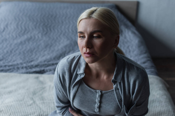 high angle view of sad blonde woman with menopause in bedroom - Foto, afbeelding