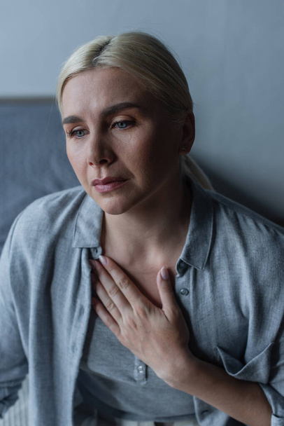 frustrated blonde woman with menopause touching chest in bedroom - Photo, Image