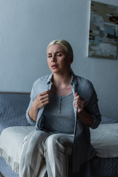 blonde woman with menopause suffering from heat and touching cardigan in bedroom - Fotoğraf, Görsel
