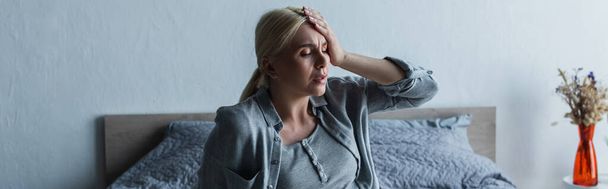 Verärgerte blonde Frau mit Migräne in den Wechseljahren im Schlafzimmer, Banner - Foto, Bild